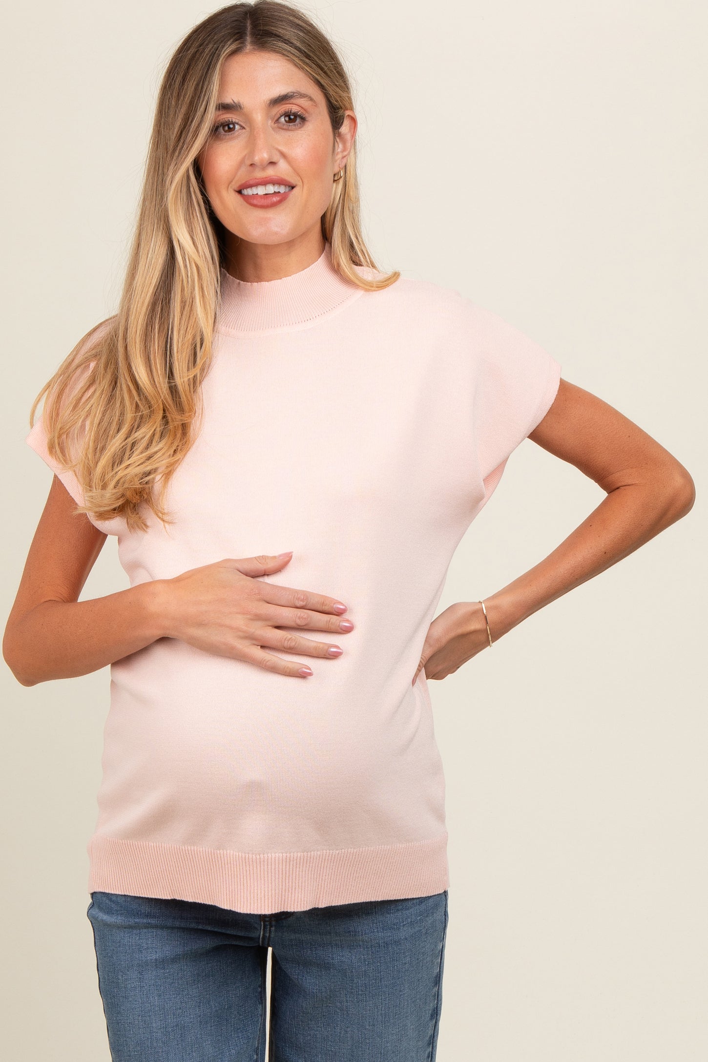 woman wearing a light pink maternity sweater with short sleeves and a visible baby bump