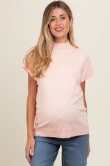 woman wearing a light pink short sleeve maternity top and showing her baby bump