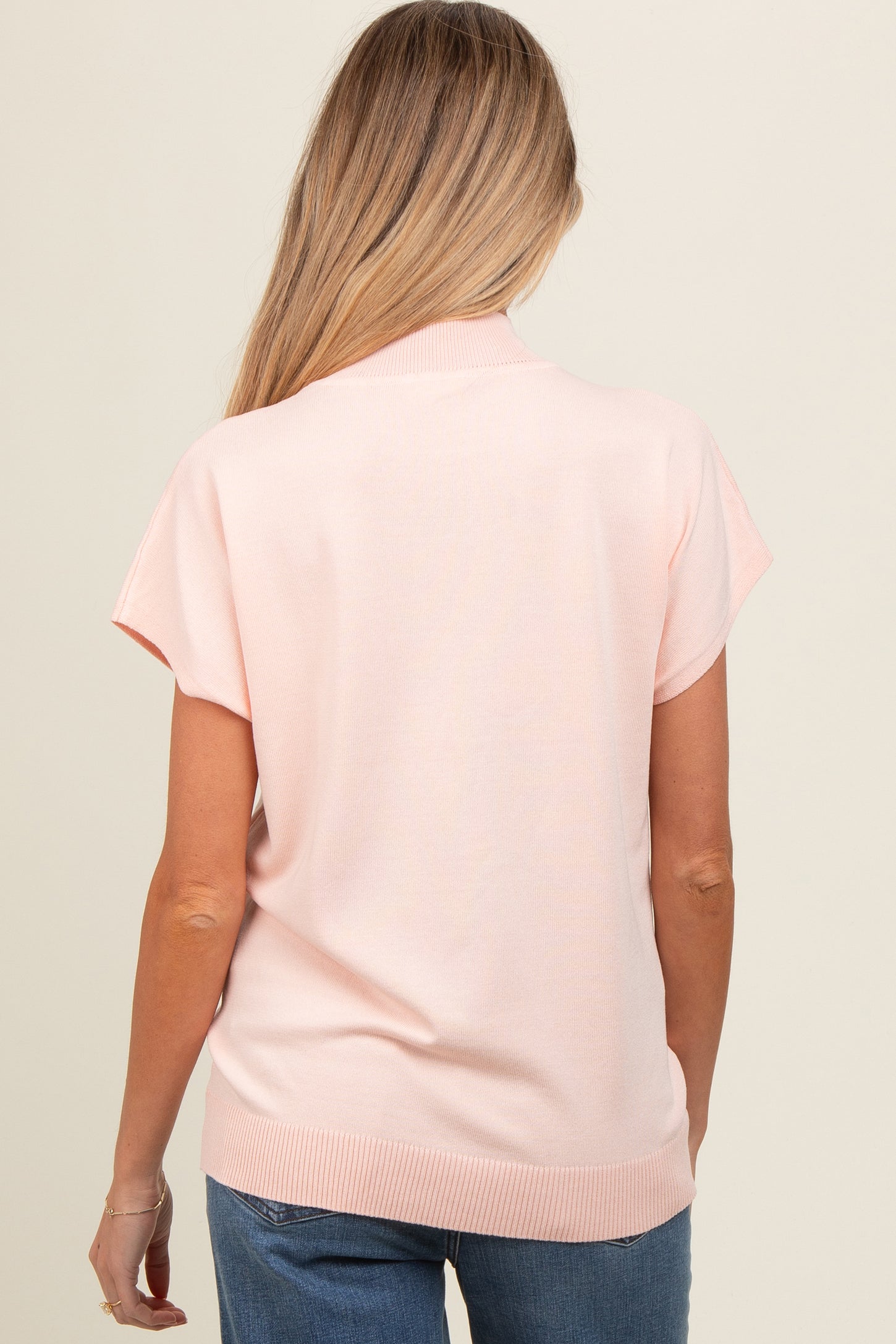 woman wearing a light pink short sleeve maternity sweater with a ribbed hem, view of the back