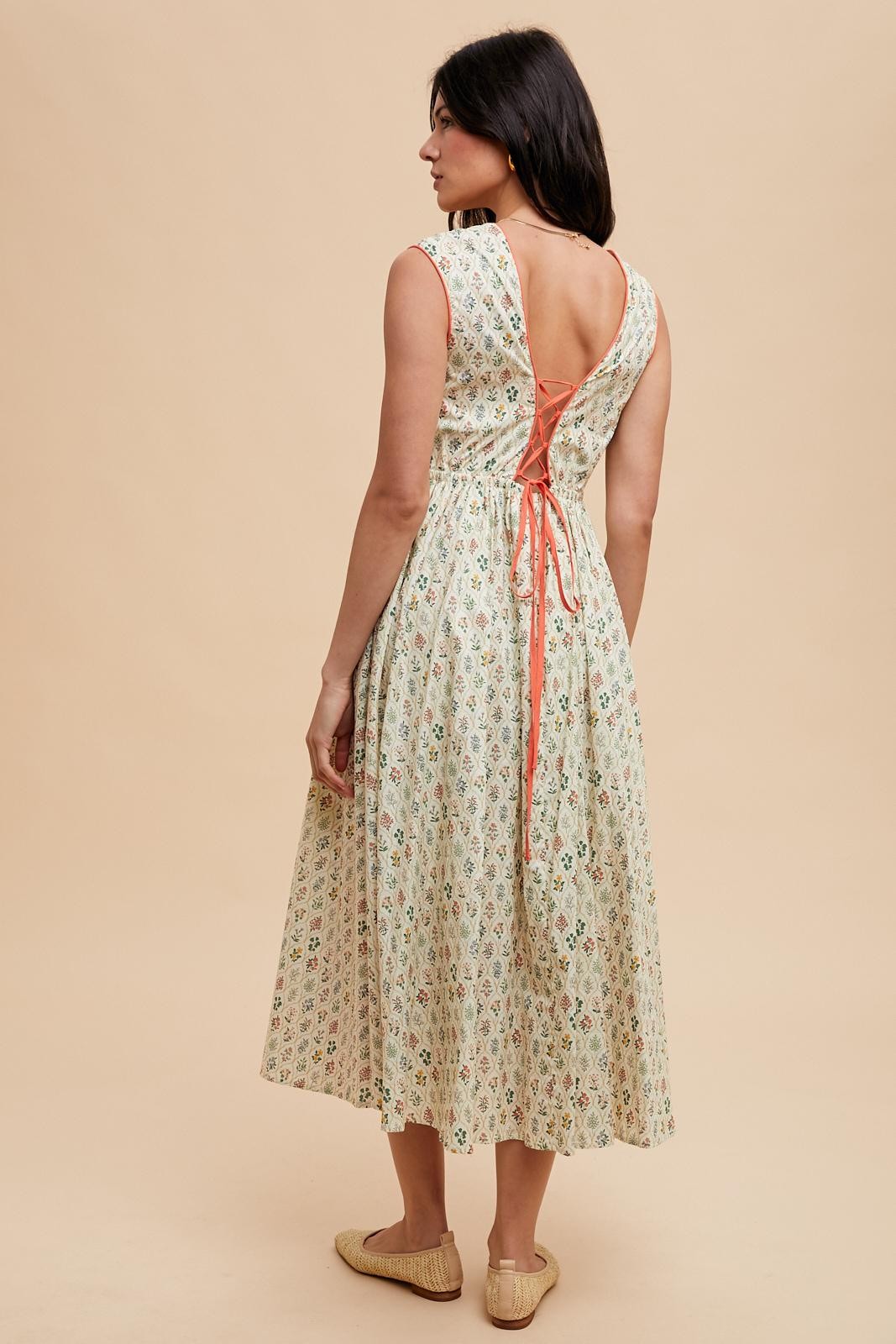 woman wearing a floral midi dress with a back tie detail and a relaxed fit, standing against a neutral background