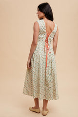 woman wearing a floral midi dress with a back tie detail and a relaxed fit, standing against a neutral background