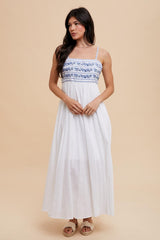 woman wearing a white maxi dress with blue embroidered detailing and thin straps
