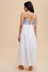 woman wearing a white maxi dress with a blue embroidered bodice and lace-up back design