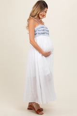 woman wearing a white maternity maxi dress with blue embroidery and holding her baby bump