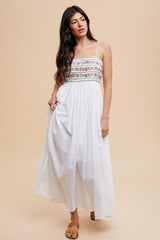 woman wearing a white maxi dress with floral embroidery on the bodice and thin spaghetti straps
