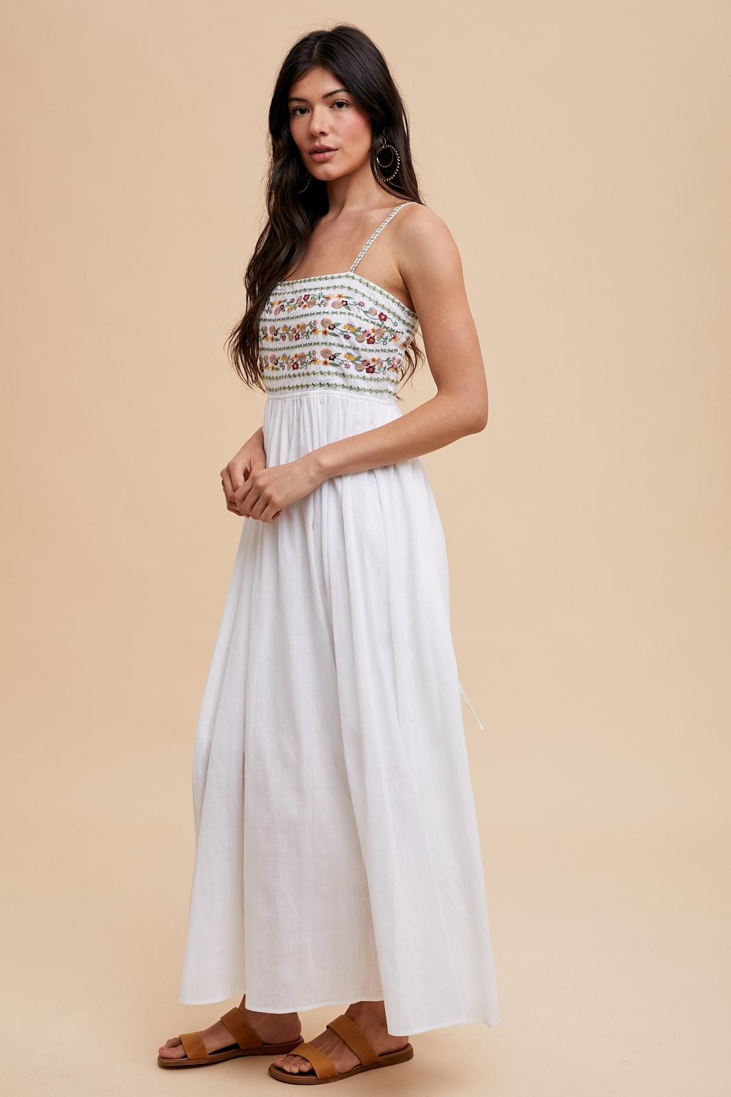 woman wearing a white embroidered maxi dress with adjustable straps and a flowy silhouette