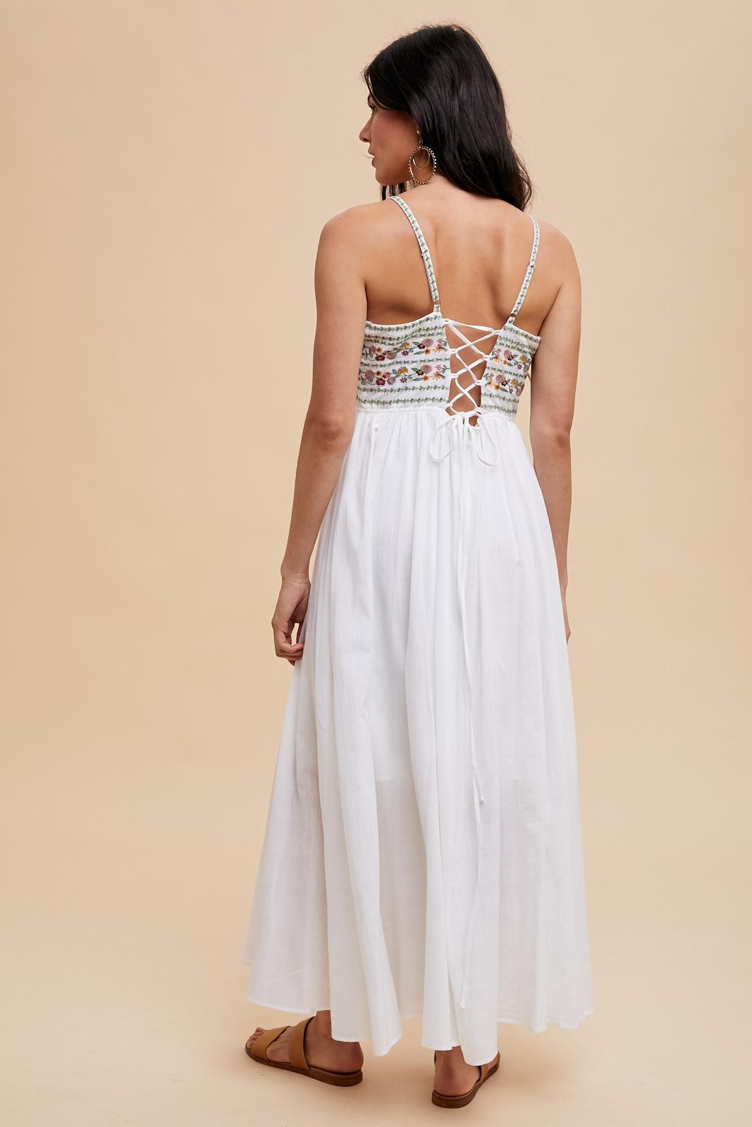 woman wearing a white maxi dress with a floral-embroidered bodice and crisscross back detail
