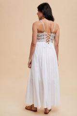 woman wearing a white maxi dress with a floral-embroidered bodice and crisscross back detail