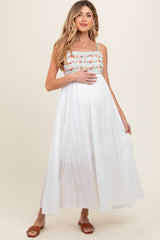 woman wearing a white maternity maxi dress with colorful embroidery and holding her baby bump