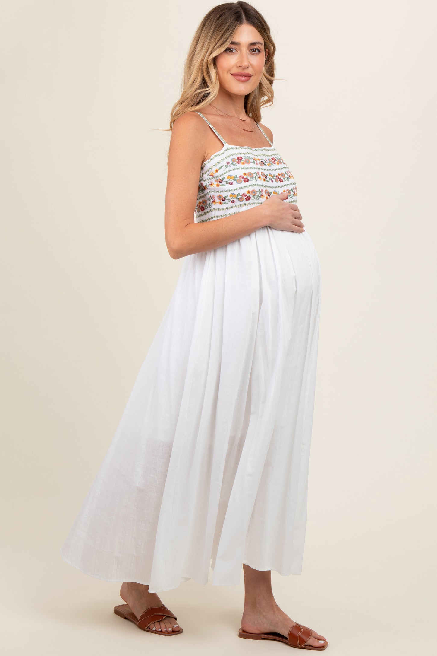 woman wearing a white floral embroidered maternity maxi dress and holding her baby bump