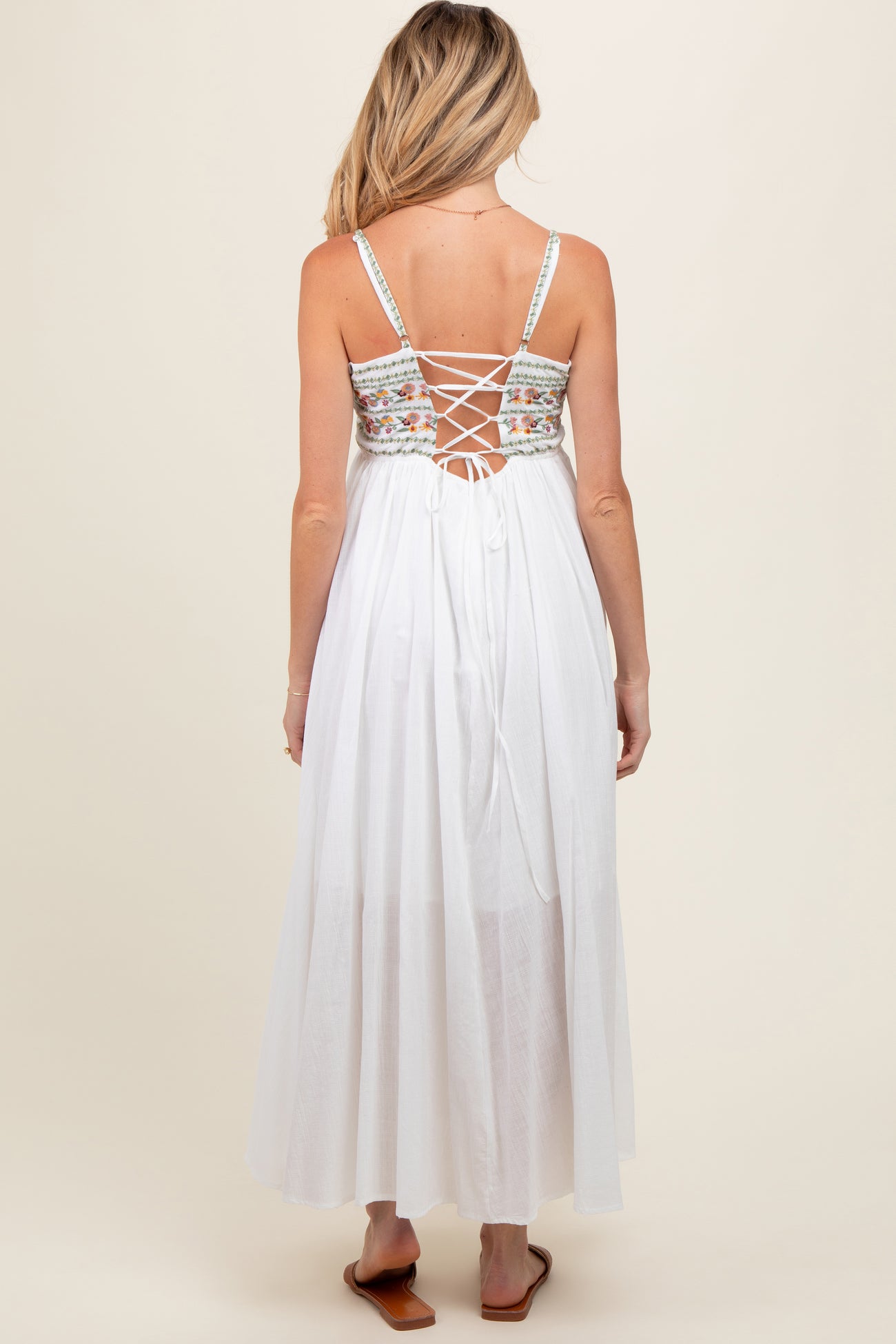 woman wearing a white maternity maxi dress with a floral embroidered back and lace-up detail