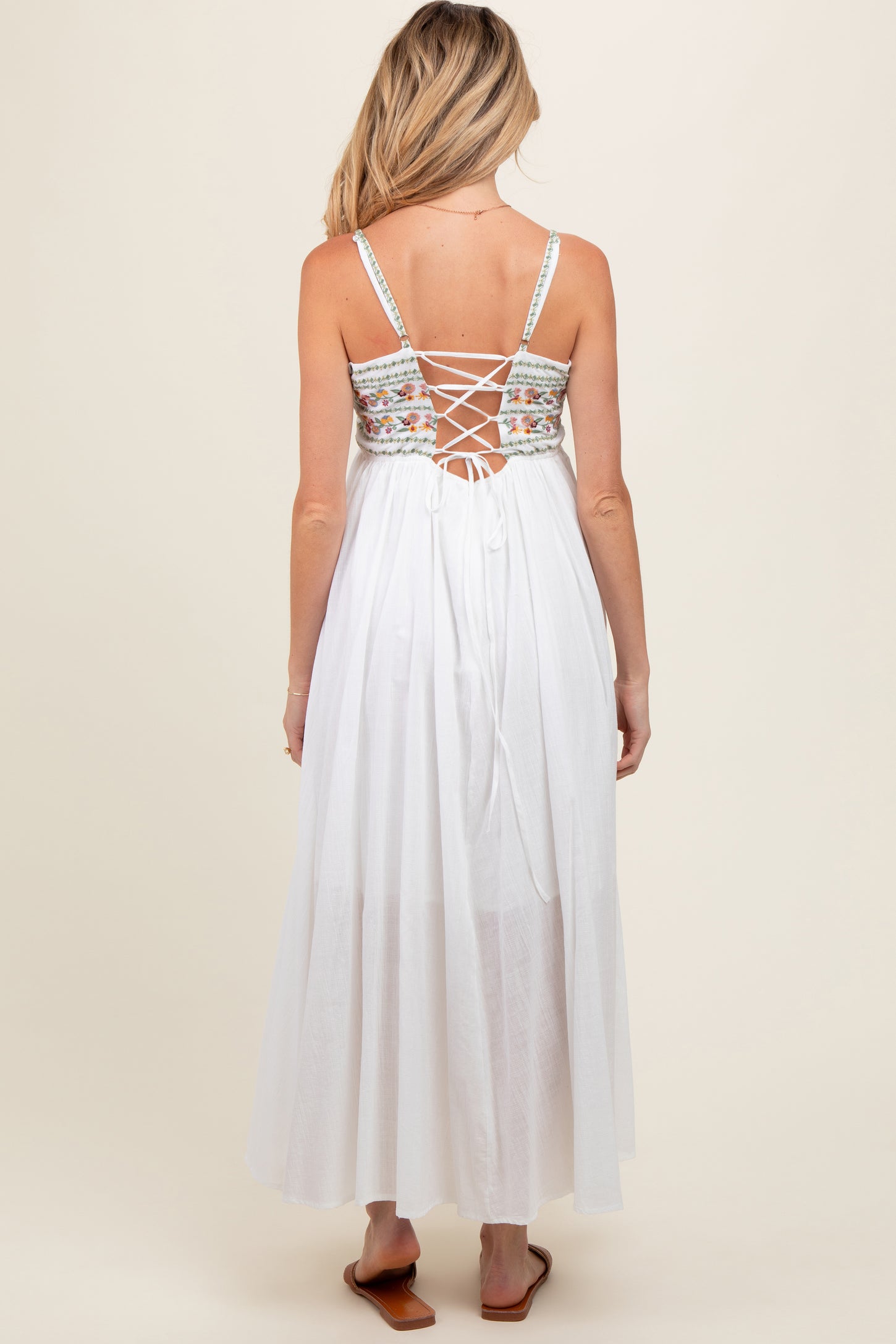 woman wearing a white maternity maxi dress with a floral embroidered back and lace-up detail