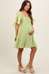 woman wearing a light green short sleeve maternity dress with a square neckline and holding her baby bump