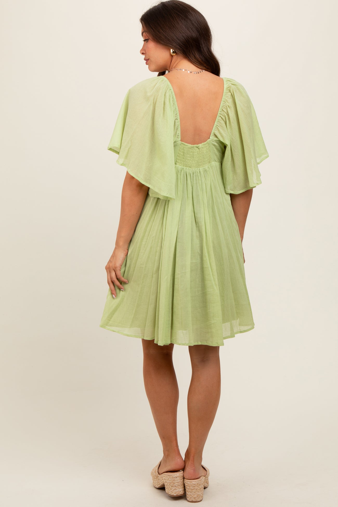 woman wearing a light green maternity dress with flutter sleeves and a scoop back
