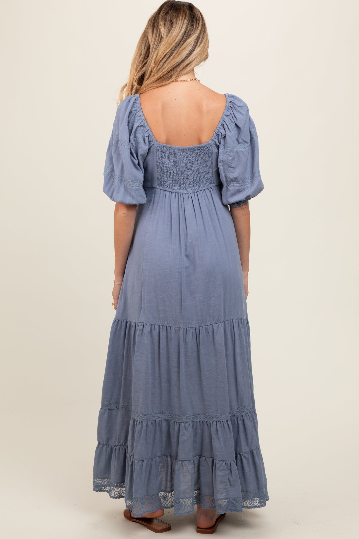 woman wearing a blue maternity maxi dress with puff sleeves and tiered ruffles, showcasing a baby bump from the back