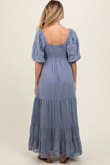 woman wearing a blue maternity maxi dress with puff sleeves and tiered ruffles, showcasing a baby bump from the back