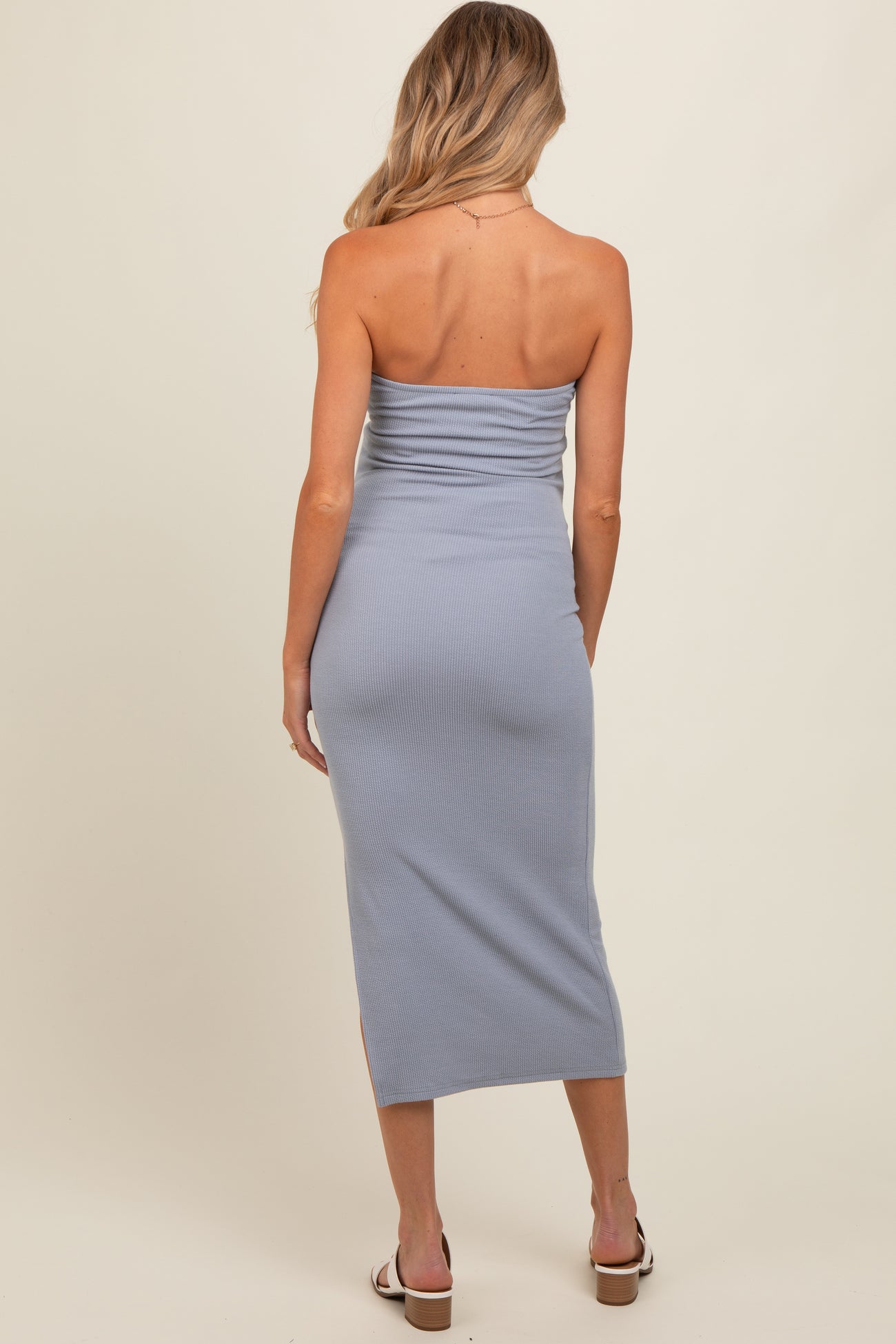 woman wearing a light blue strapless maternity dress with a fitted silhouette and side slits, showing a baby bump