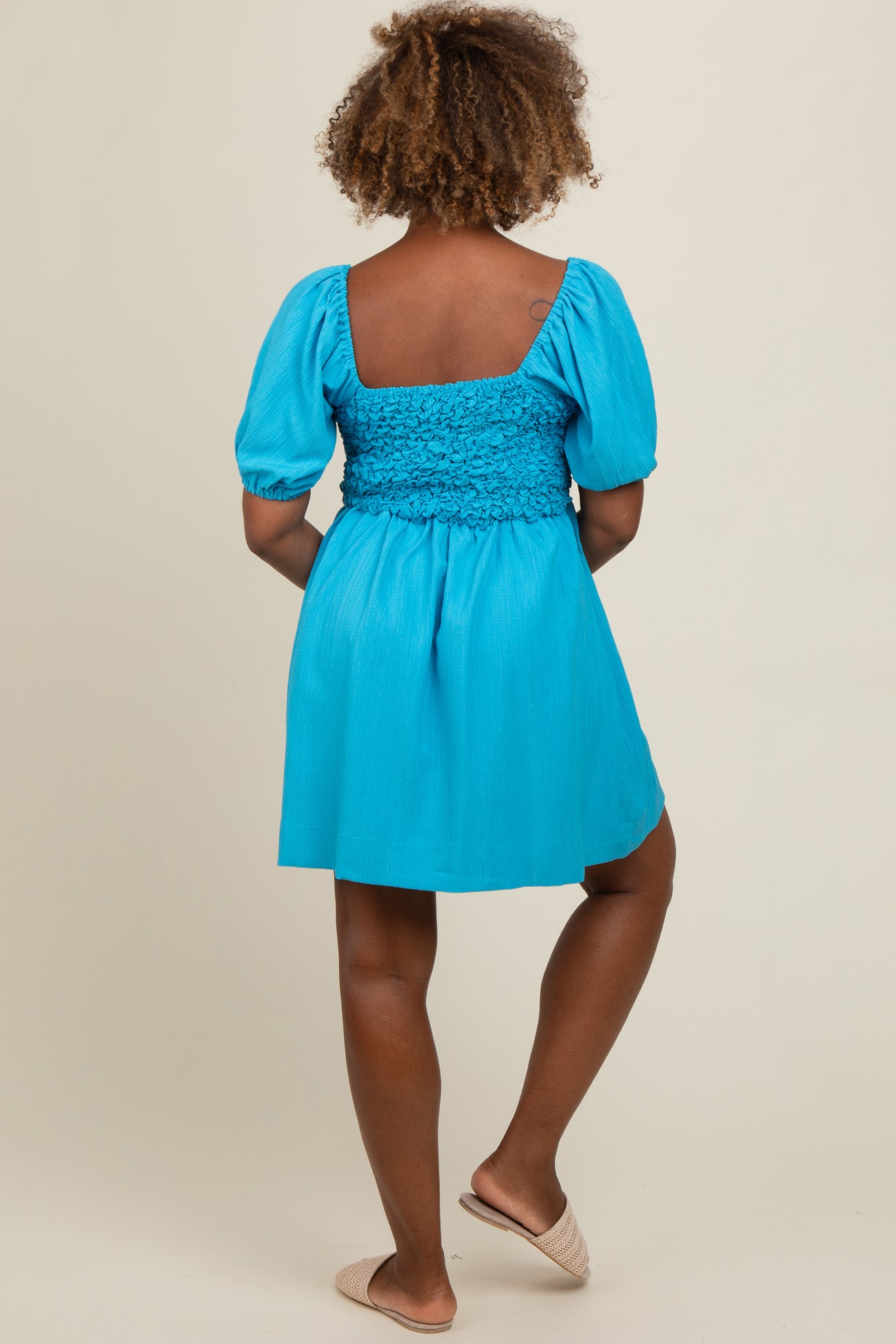 woman wearing a bright blue puff sleeve dress with a smocked bodice and a flared skirt, shown from the back.