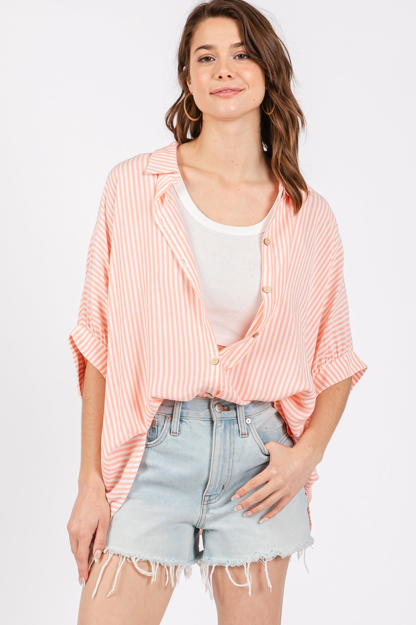 woman wearing a coral and white striped oversized button-up shirt with rolled sleeves and distressed denim shorts