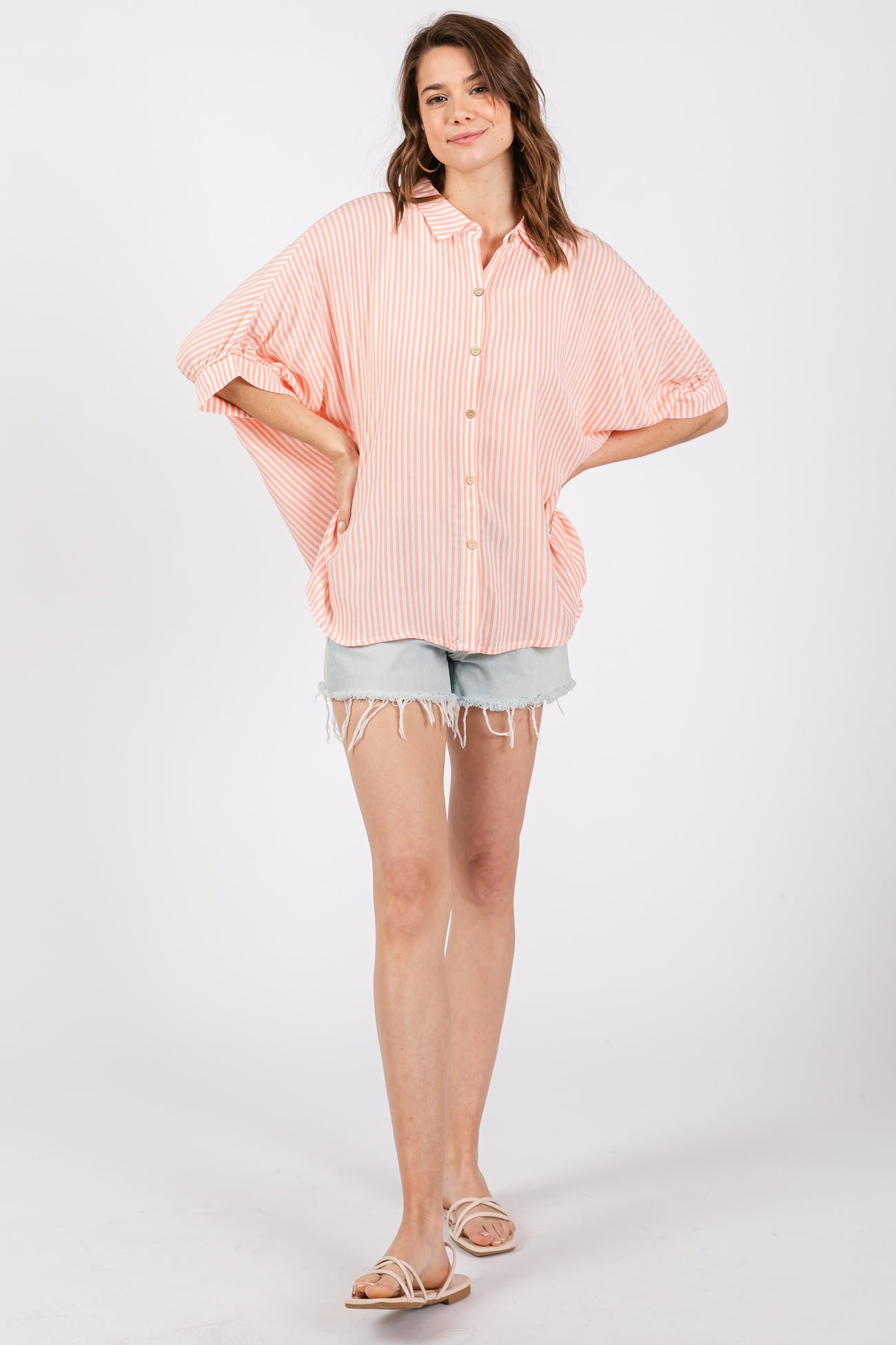 woman wearing a pink and white striped oversized button-down shirt with rolled sleeves and denim shorts