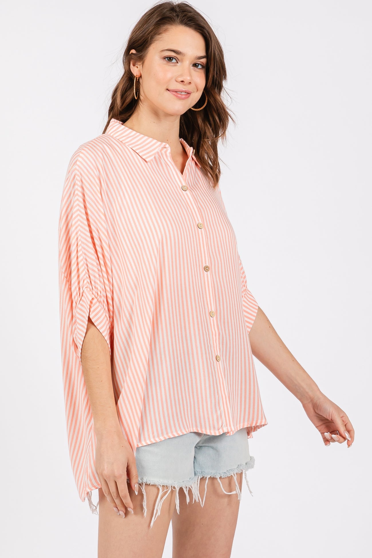 woman wearing a coral and white striped button-up shirt with short sleeves and distressed denim shorts