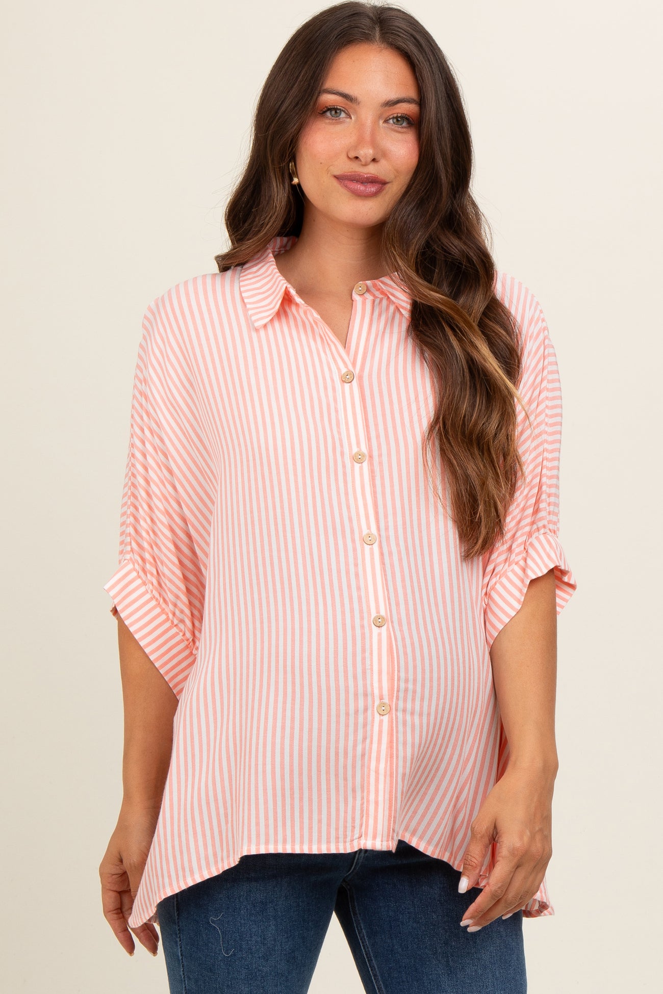 woman wearing a pink and white striped maternity button-up shirt with rolled sleeves and a relaxed fit