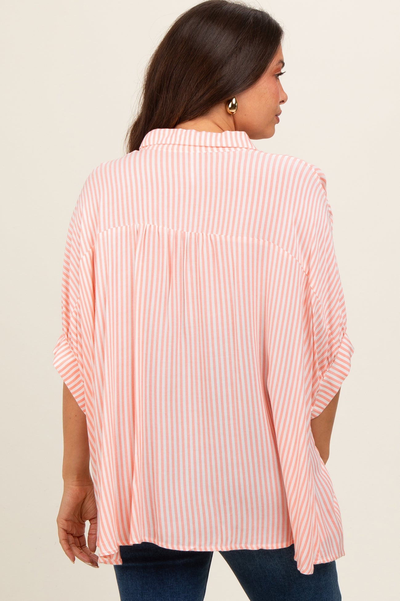 woman wearing a pink and white striped maternity top with a loose fit and rolled sleeves, showing the back view