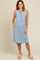 woman wearing a light wash sleeveless denim dress with a button-down front and frayed hem, displaying side pockets