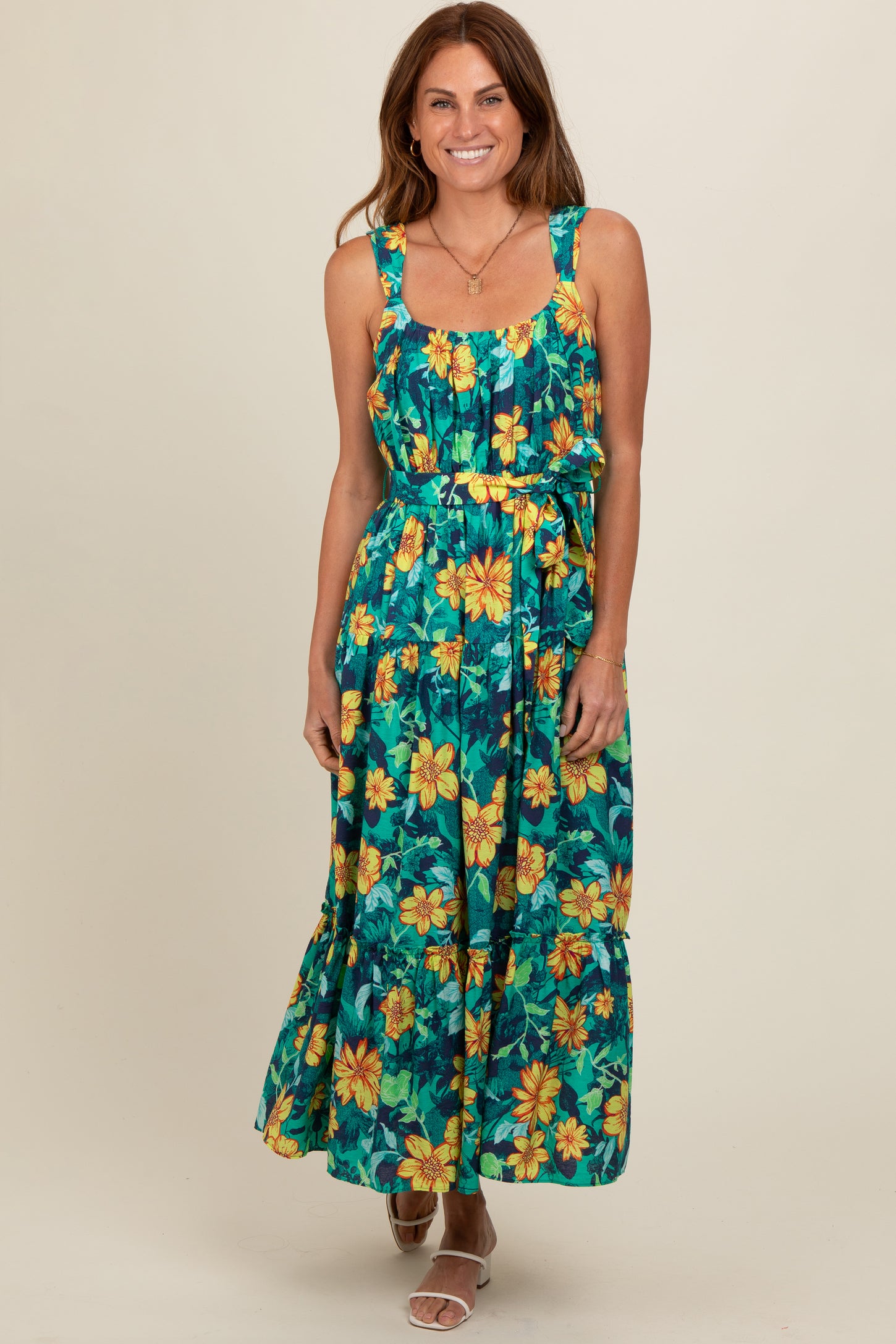 woman wearing a sleeveless green floral maxi dress with yellow flowers and a tiered skirt, smiling at the camera