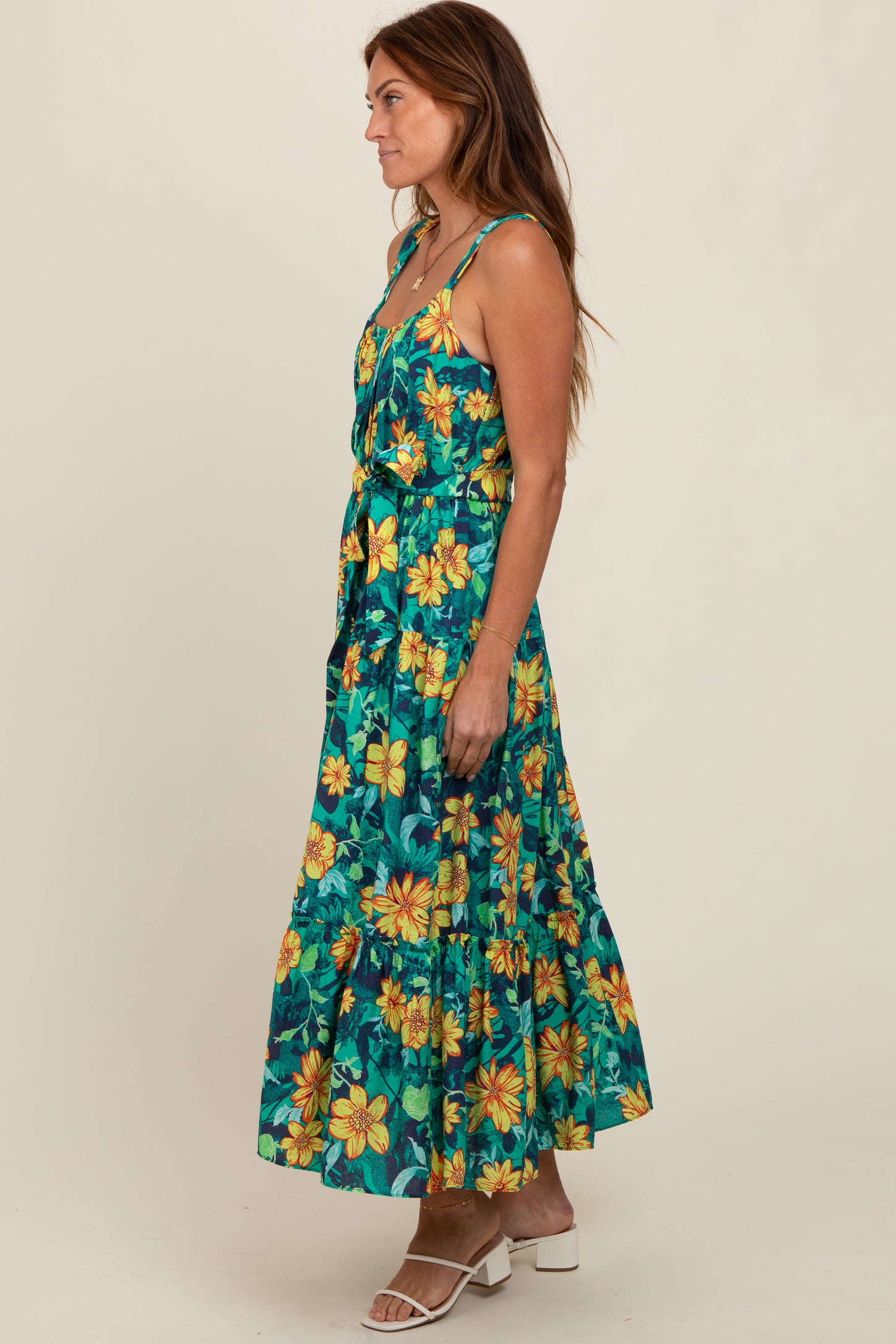 woman wearing a floral maxi dress with yellow and green patterns and a tiered skirt, styled with white sandals