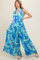 woman wearing a blue and green abstract print maternity jumpsuit with a halter neck and wide legs