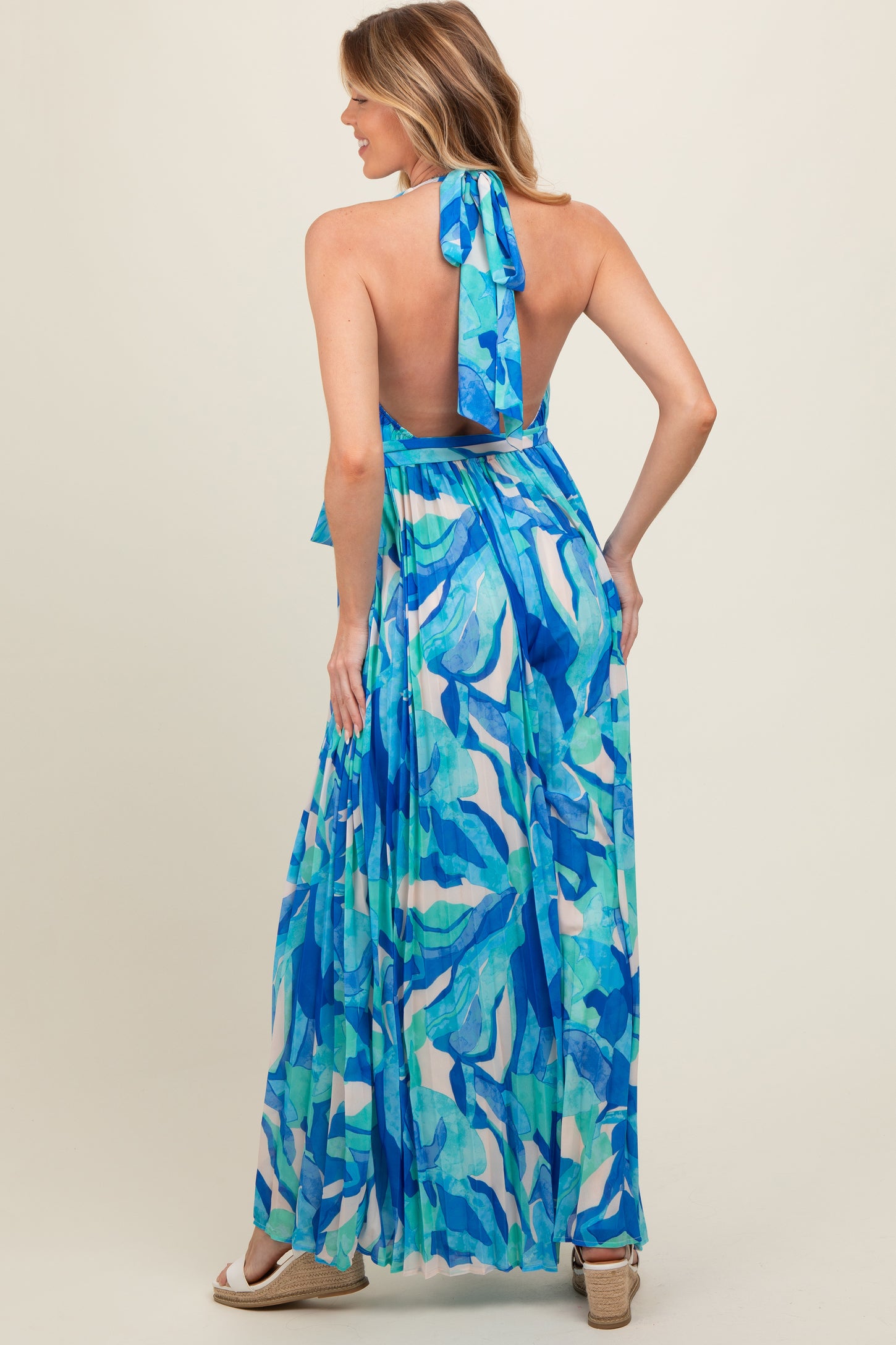 woman wearing a blue and green patterned halter neck maternity maxi dress, showing a bare back with a flowing skirt