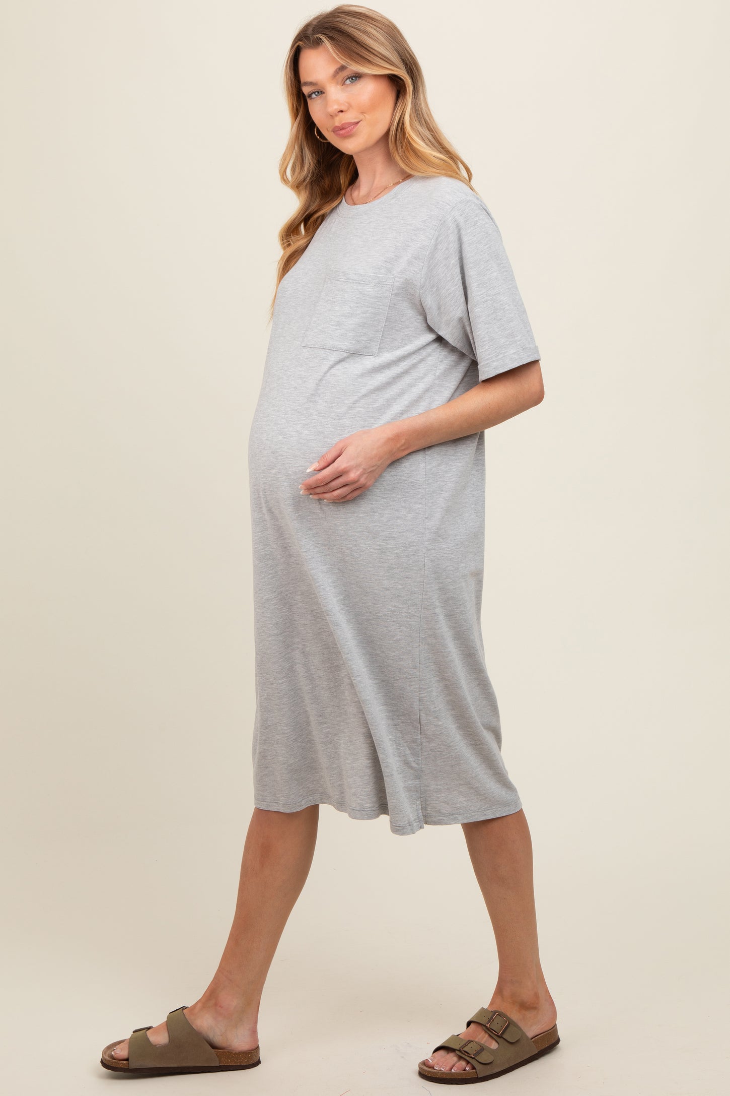 woman wearing a gray short sleeve maternity dress showing her baby bump and standing in a relaxed pose