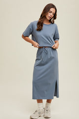 woman wearing a blue midi t-shirt dress with short sleeves and a drawstring waist, standing with hands at the waist