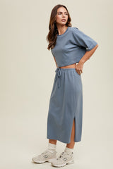 woman wearing a blue crop top and matching midi skirt with side slits, styled with white sneakers