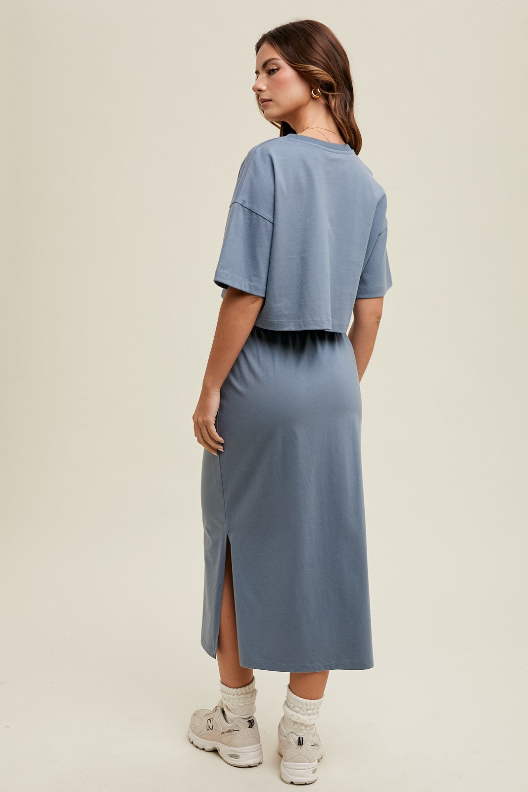woman wearing a gray-blue cropped t-shirt and a matching midi dress with a side slit, seen from the back
