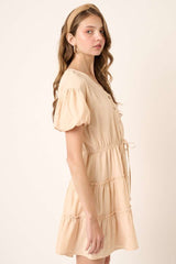woman wearing a blush puff sleeve mini dress with buttons and a tie waist detail