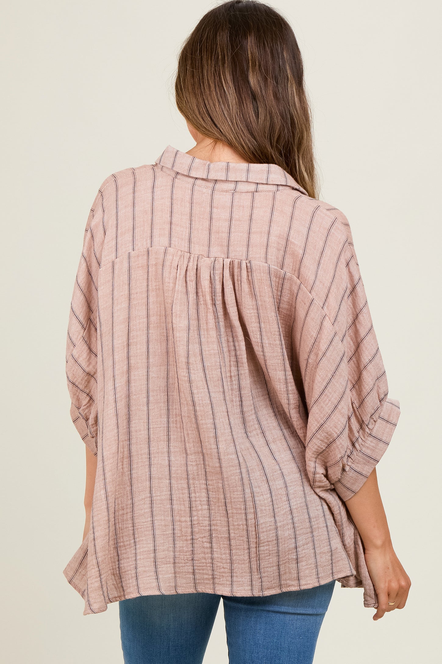 woman wearing a blush striped maternity top with rolled sleeves, showing her back and a flowing fit over her baby bump