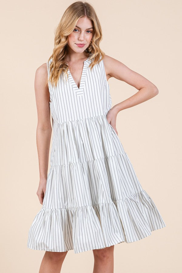 woman wearing a white and navy striped sleeveless tiered dress with a v-neckline