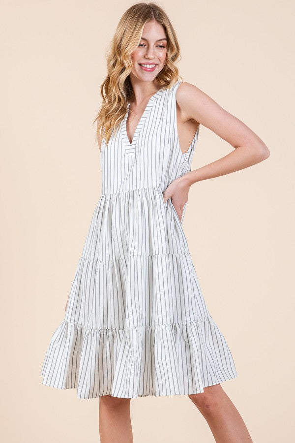 woman wearing a white and navy striped sleeveless tiered dress with a v-neckline and flowy silhouette