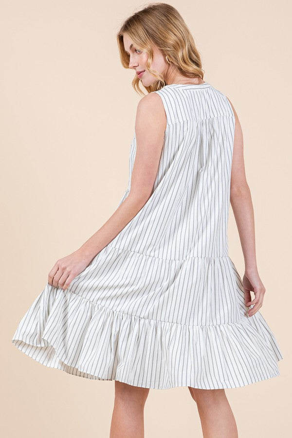 woman wearing a sleeveless white and gray striped tiered dress, twirling to show the flared hem and relaxed fit