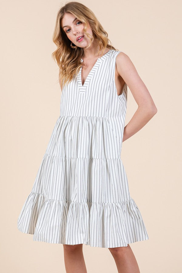 woman wearing a white and black striped sleeveless tiered dress with a v-neckline and relaxed fit
