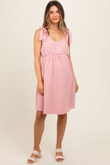 woman wearing a light pink maternity dress with tie straps and an empire waist, featuring a relaxed fit