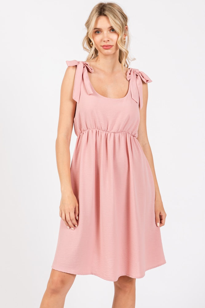 woman wearing a light pink sleeveless dress with tie shoulder straps and a smocked waist