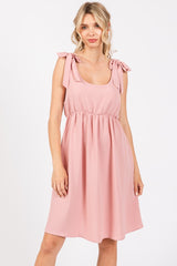 woman wearing a light pink sleeveless dress with tie shoulder straps and a smocked waist