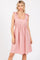 woman wearing a light pink sleeveless dress with tie shoulder straps and a smocked waist