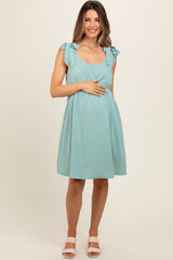 woman wearing a teal maternity dress with tie sleeves and holding her baby bump