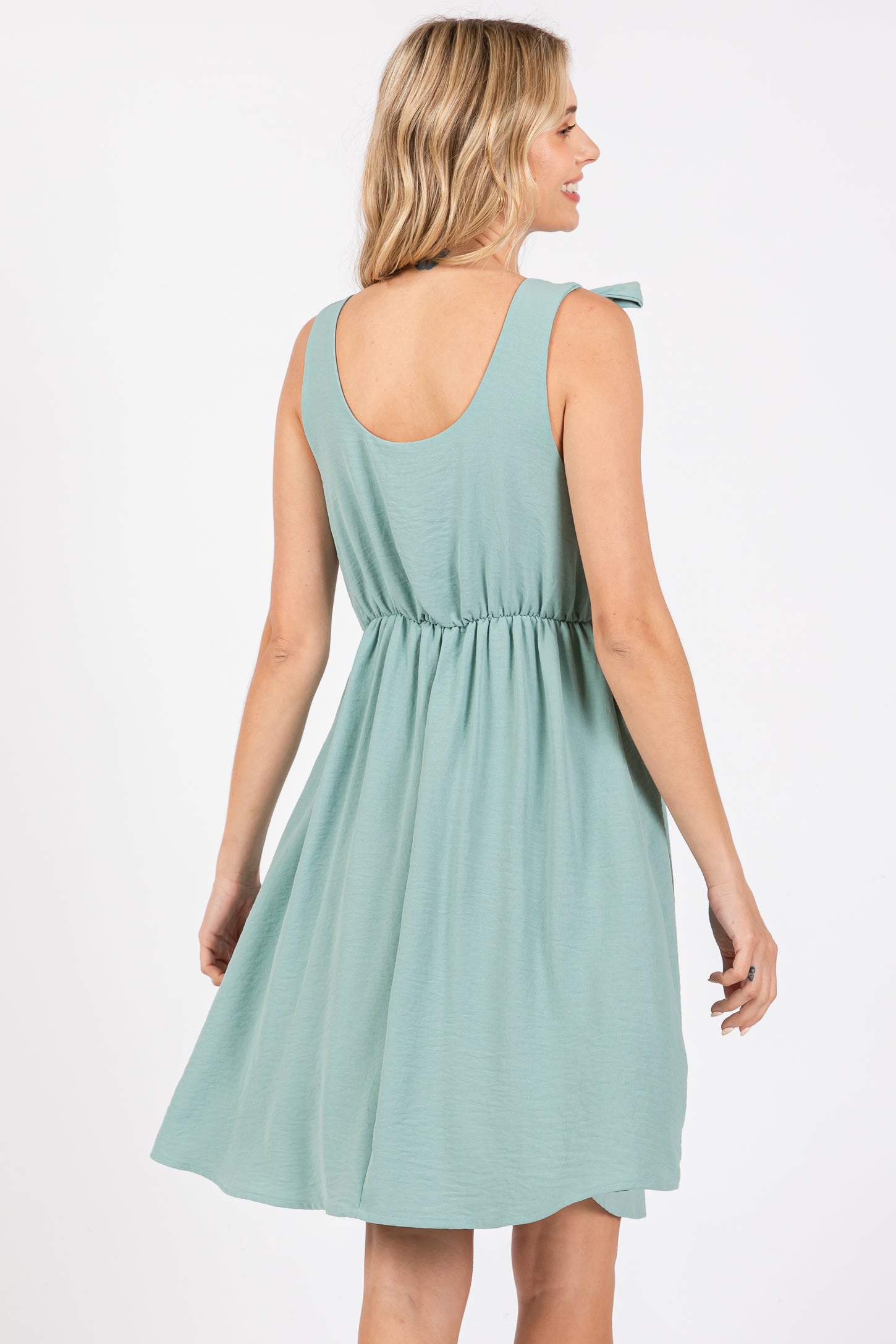 woman wearing a mint green sleeveless dress with a tie detail on the shoulder and a cinched waist