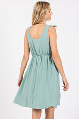 woman wearing a mint green sleeveless dress with a tie detail on the shoulder and a cinched waist