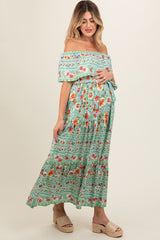 woman wearing a green floral off-the-shoulder maternity maxi dress and holding her baby bump